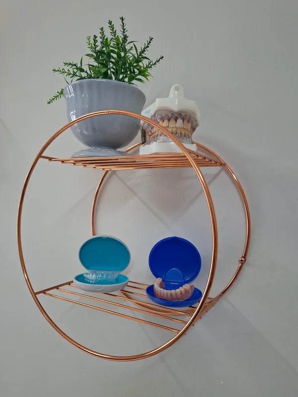 Prateleira circular cobre no consultório, com planta, modelo de arcada e estojos de aparelho